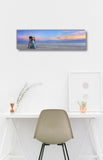 a serene beach scene with a lifeguard chair overlooking the ocean, a white desk with a plant and a candle, and a framed picture on the wall.